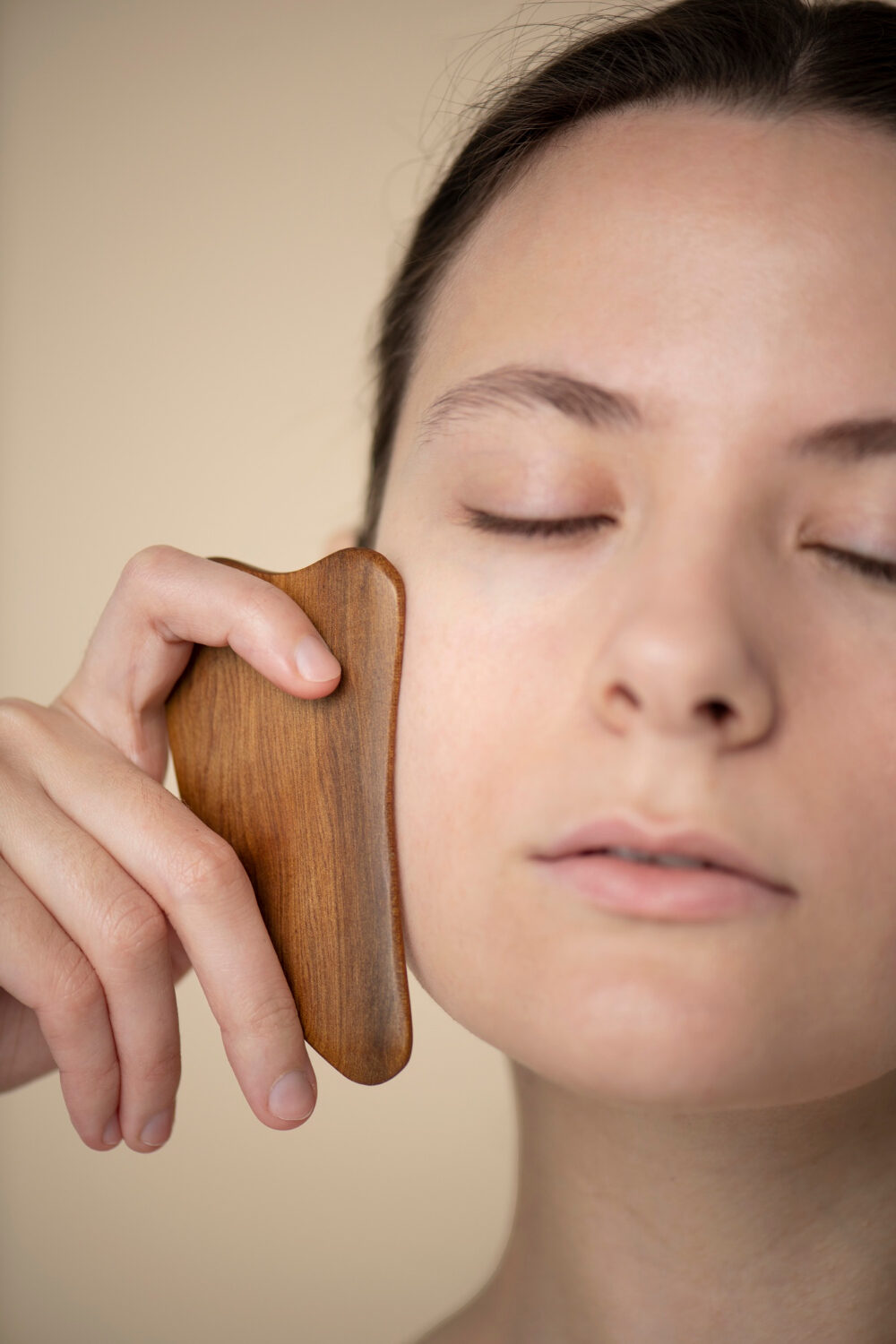 a woman using a wooden gua sha tool on her face for facial massage and relaxation