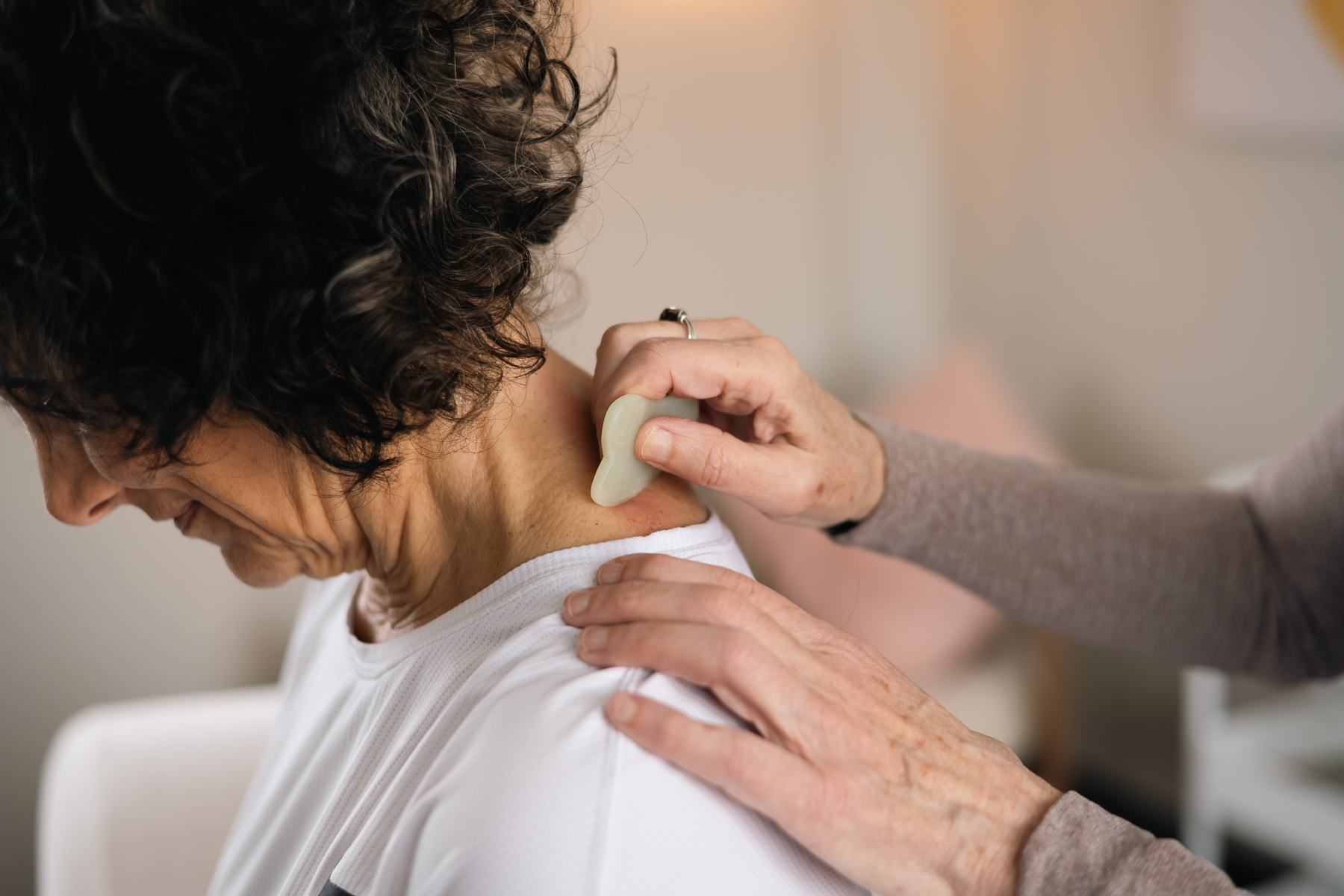 A person performing gua sha therapy on another individual's neck and shoulder using a jade tool