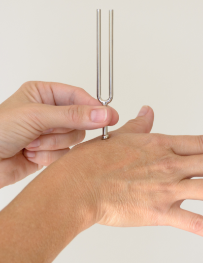 A tuning fork pressed against the back of a hand, used for therapeutic purposes