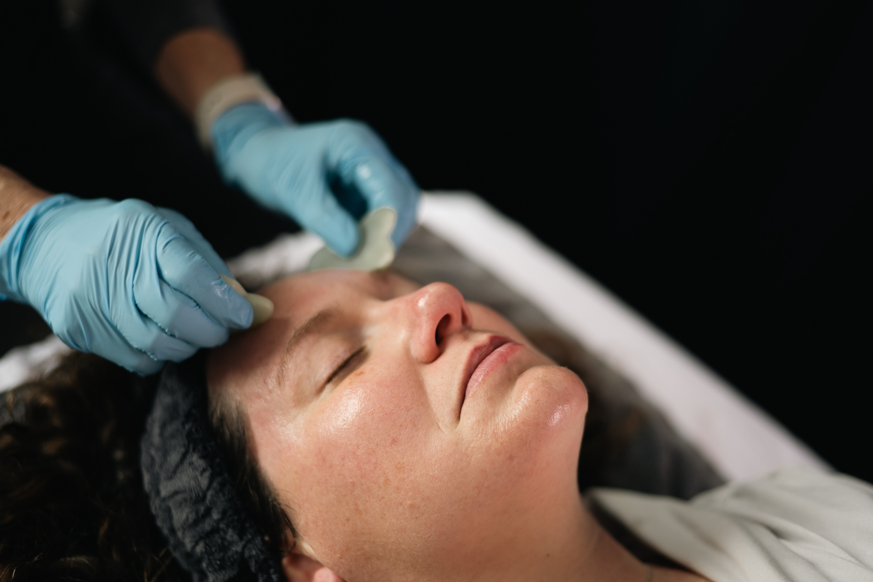 A facial gua sha treatment on a relaxed woman