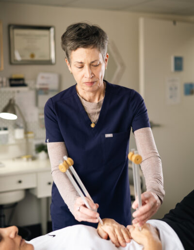 A practitioner performing sound therapy with tuning forks on a patient’s hands